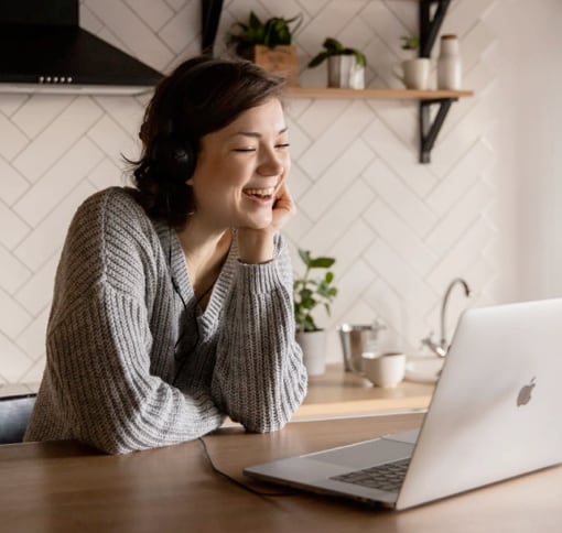 A white woman sitting at a table, looking at the open screen of the laptop infront of her.